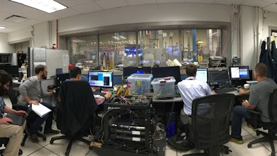 University of Colorado and Air Force Research Lab teams in the control room during a dual-mode ramjet ground test. The modified dual frequency comb system is in the center foreground, and is sending light to the test cell, which is located beyond the control room windows.