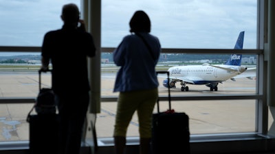 In this Tuesday, May 25, 2021, file photo, travelers watch a JetBlue Airways aircraft taxi away from a gate at Ronald Reagan Washington National Airport†ahead of Memorial Day weekend.
