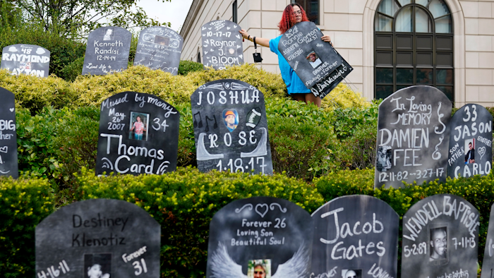 Jayde Newton helps to set up cardboard gravestones with the names of victims of opioid abuse outside the courthouse where the Purdue Pharma bankruptcy is taking place in White Plains, N.Y., Monday, Aug. 9, 2021. Purdue Pharma's quest to settle thousands of lawsuits over the toll of OxyContin is entering its final phase with the grudging acceptance of most of those with claims against the company.