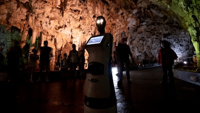 Persephone guides the visitors inside Alistrati cave, about 135 kilometers (84 miles) northeast of Thessaloniki, Greece, Monday, Aug. 2, 2021. Persephone, billed as the world's first robot used as a tour guide inside a cave, has been welcoming visitors to the Alistrati cave, since mid-July.