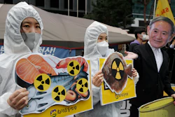 In this April 13, 2021, file photo, environmental activists wearing a mask of Japanese Prime Minister Yoshihide Suga and protective suits perform to denounce the Japanese government's decision to release treated radioactive Fukushima water, near the Japanese Embassy in Seoul, South Korea. Japan’s government adopted an interim plan Tuesday, Aug. 24, 2021 that it hopes will win support from fishermen and other concerned groups for a planned release into the sea of treated but still radioactive water from the wrecked Fukushima nuclear plant.