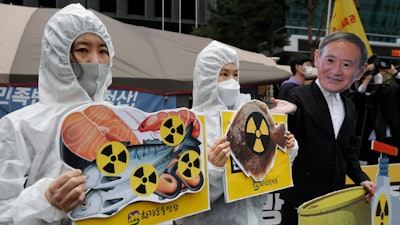 In this April 13, 2021, file photo, environmental activists wearing a mask of Japanese Prime Minister Yoshihide Suga and protective suits perform to denounce the Japanese government's decision to release treated radioactive Fukushima water, near the Japanese Embassy in Seoul, South Korea. Japan’s government adopted an interim plan Tuesday, Aug. 24, 2021 that it hopes will win support from fishermen and other concerned groups for a planned release into the sea of treated but still radioactive water from the wrecked Fukushima nuclear plant.