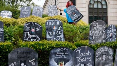 Jayde Newton helps to set up cardboard gravestones with the names of victims of opioid abuse outside the courthouse where the Purdue Pharma bankruptcy is taking place in White Plains, N.Y., Monday, Aug. 9, 2021. Purdue Pharma's quest to settle thousands of lawsuits over the toll of OxyContin is entering its final phase with the grudging acceptance of most of those with claims against the company.