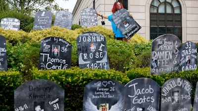 Jayde Newton helps to set up cardboard gravestones with the names of victims of opioid abuse outside the courthouse where the Purdue Pharma bankruptcy is taking place in White Plains, N.Y., Monday, Aug. 9, 2021. Purdue Pharma's quest to settle thousands of lawsuits over the toll of OxyContin is entering its final phase with the grudging acceptance of most of those with claims against the company.