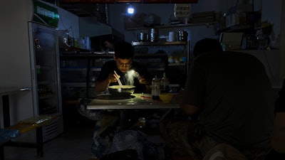 A man uses his smartphone flashlight to light up his bowl of noodles as he eats his breakfast at a restaurant during a blackout in Shenyang in northeastern China's Liaoning Province, Wednesday, Sept. 29, 2021. People ate breakfast by flashlight and shopkeepers used portable generators Wednesday as power cuts imposed to meet official conservation goals disrupted manufacturing and daily life.