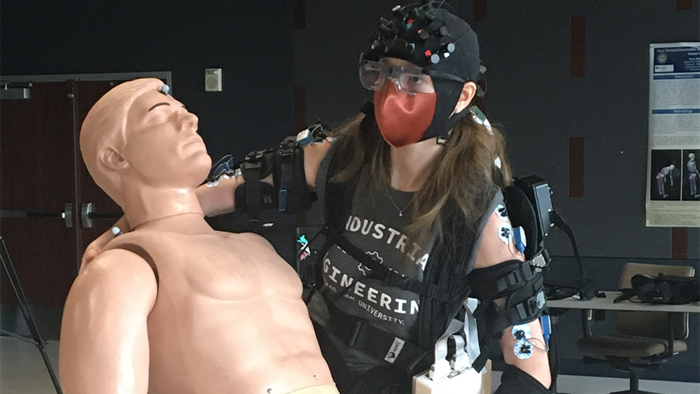 Doctoral student Sarah Hopko is wearing an exoskeleton while performing patient handling tasks. Her brain activity is being tracked using Near Infrared Spectroscopy, gaze behavior is being tracked using eye tracking and muscle activity through electromyographic sensors.