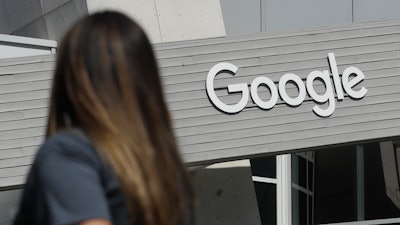 In this Sept. 24, 2019, file photo, a woman walks below a Google sign on the campus in Mountain View, Calif. Google on Thursday, Oct. 7, 2021, will no longer allow digital ads promoting false climate change claims to appear next to the content of other publishers, hoping to deny money to those making such claims and to stop the spread of misinformation on its platform.