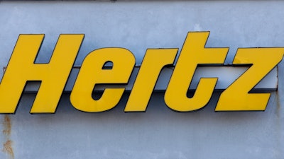 In this Tuesday, Nov. 28, 2017 photo a Hertz rental car logo rests on the front of a Hertz location, in Boston. Car rental company Hertz is ordering 100,000 electric vehicles from Tesla. The company says it’s buying the Tesla Model 3s by the end of 2022, and it also will buy electric vehicle chargers.