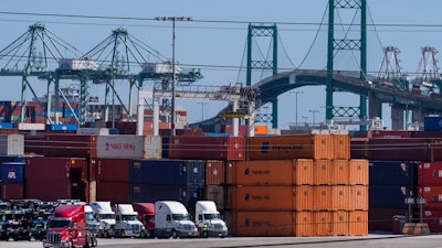 In this Tuesday, Oct. 19, 2021, photo trucks line up next to containers at the Port of Los Angeles in san Pedro, Calif. The Vincent Thomas Bridge suspension bridge, crossing the Los Angeles Harbor links San Pedro with Terminal Island. California Gov. Gavin Newsom on Wednesday, Oct. 20, 2021 issued an order that aims to ease bottlenecks at the ports of Los Angeles and Long Beach that have spilled over into neighborhoods where cargo trucks are clogging residential streets. Last week the White House allowed the ports complex to become a 24-hour operation in an effort to break the logjam and reduce shipping delays.