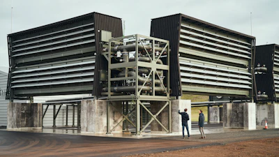 In this September 2021 image provided by Climeworks AG, CEOs Jan Wurzbacher and Christoph Gebald appear in front of an air-scrubbing machine where fans suck air into big, black collection boxes where the carbon dioxide accumulates on a filter at Climeworks’ Orca plant near Reykjavik, Iceland. The Iceland plant is the largest such facility in the world, capturing about 4,000 metric tons of carbon dioxide per year.