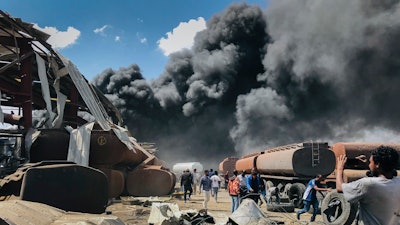 People are seen in front of clouds of black smoke from fires in the aftermath at the scene of an airstrike in Mekele, the capital of the Tigray region of northern Ethiopia on Oct. 20, 2021. A year after war began there, the findings of the only human rights investigation allowed in Ethiopia's blockaded Tigray region will be released Wednesday, Nov. 3, 2021.