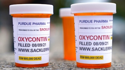In this Aug. 9, 2021, file photo, fake pill bottles with messages about OxyContin maker Purdue Pharma are displayed during a protest outside the courthouse where the bankruptcy of the company is taking place in White Plains, N.Y. A federal judge should reject a sweeping settlement to thousands of lawsuits against OxyContin maker Purdue Pharma, a group of states said at a hearing Tuesday, Nov. 30, 2021 arguing that the protections it extends to members of the Sackler family who own the firm are improper.