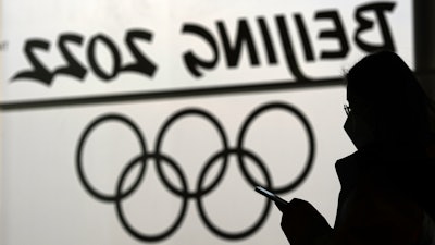 A woman looks at her phone as she passes an Olympic logo inside the main media center for the Beijing Winter Olympics, Jan. 18, 2022.