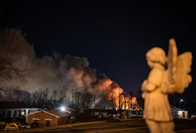 An angel statue faces in the direction of billowing smoke from a fire at the Weaver Fertilizer Plant on Monday, Jan. 31, 2022, in Winston-Salem, N.C.