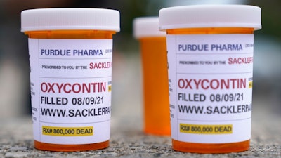 Fake pill bottles with messages about OxyContin maker Purdue Pharma are displayed during a protest outside the courthouse where the bankruptcy of the company is taking place in White Plains, N.Y., on Aug. 9, 2021. A judge said he is extending legal protections for members of the Sackler family, Wednesday, March 2, 2022, who own OxyContin maker Purdue Pharma by another three weeks to buy time to work out a new settlement to thousands of lawsuits over the opioid crisis.