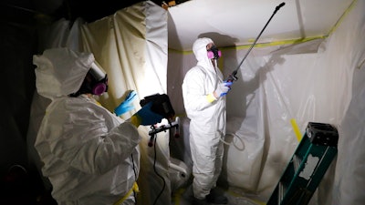 Asbestos Removal Technologies Inc., job superintendent Ryan Laitila, right, sprays amended water as job forman Megan Eberhart holds a light during asbestos abatement in Howell, Mich., Oct. 18, 2017. The Environmental Protection Agency on Tuesday, April 5, 2022, proposed a rule to finally ban asbestos, a carcinogen that is still used in some chlorine bleach, brake pads and other products and kills thousands of Americans every year.