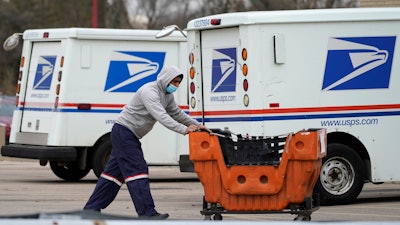 A United States Postal Service employee works outside a post office in Wheeling, Ill., Dec. 3, 2021. Four environmental groups that want the U.S. Postal Service to buy more electric delivery vehicles are suing to halt further purchases. The lawsuit, filed Thursday, April 28, 2022, in federal court in California, asks a judge to order the Postal Service to conduct a more thorough environmental review before moving forward with the next-generation vehicle program.