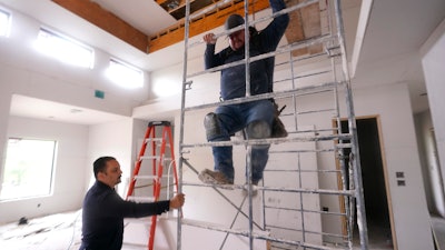 Joshua Correa, left, steadies a scaffolding for Samuel as they work at a home under construction in Plano, Texas, May 3, 2022.