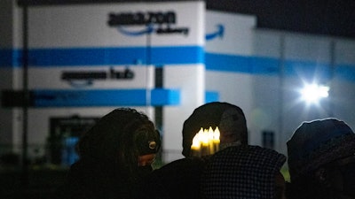 A person holds six electric candles symbolizing the six workers who died while working at the Edwardsville Amazon site in the background, during a vigil, Friday, Dec. 17, 2021, in Edwardsville, Ill., after part of the building collapsed due to a tornado the previous week before.