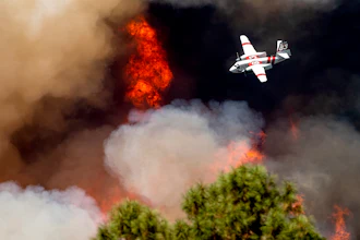 An air tanker flies past flames while battling the Oak Fire in Mariposa County, Calif., Sunday, July 24, 2022. Wildfires, floods and soaring temperatures have made climate change real to many Americans. Yet a sizeable number continue to dismiss the scientific consensus that human activity is to blame. That's in part because of a decades-long campaign by fossil fuel companies to muddy the facts and promote fringe explanations.