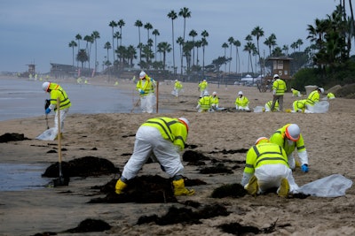 Workers in protective suits clean the contaminated beach in Corona Del Mar after an oil spill off the Southern California coast, on Oct. 7, 2021. The Orange County Board of Supervisors on Tuesday, July 26, 2022, agreed to accept a proposed claim settlement with Amplify Energy Corp, the owner of an underwater oil pipeline that spilled some 25,000 gallons of crude into the ocean.