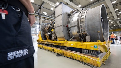 Employees stand around the turbine serviced in Canada for the Nordstream 1 natural gas pipeline in Muelheim an der Ruhr, Germany, Aug. 3, 2022. German Chancellor Olaf Scholz visited a plant by Siemens Energy where a turbine, which is at the center of a dispute between Germany and Russia over reduced gas supplies, is currently sitting in storage until it can be shipped to Russia.