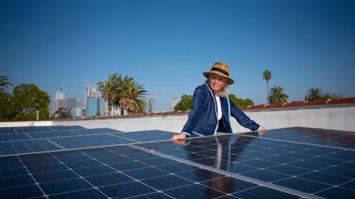 In this image provided by Ben Gibbs, Wendy Schmidt visits a community solar installation atop the roof of an Esperanza Community Housing apartment building, across the street from an oil drilling site in South Central Los Angeles on Nov. 3, 2021. The Schmidt Family Foundation funded the installation of the solar panels in 2017 so tenants could directly access renewable energy.