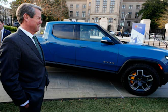 Georgia Gov. Brian Kemp smiles as he stands next to a Rivian electric truck during a ceremony to announce that the electric truck maker plans to build a $5 billion battery and assembly plant east of Atlanta projected to employ 7,500 workers, on Dec. 16, 2021, in Atlanta.