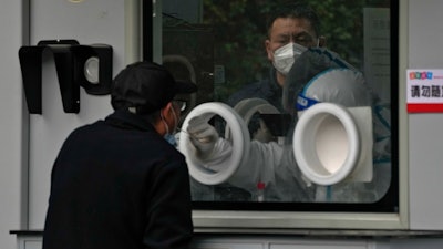 A man wearing face mask waits in line as a worker in protective suit collects a sample from a man at a coronavirus testing site in Beijing, Wednesday, Nov. 9, 2022.