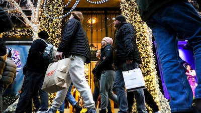 Shoppers carry shopping bags down Fifth Avenue, Monday, Dec. 19, 2022, in New York. After a two-year hiatus, holiday procrastinators are back this year, during a holiday season when retailers need them even more. Shoppers have been pulling back on buying and waiting for the best deals as inflation weighs on their shopping habits.