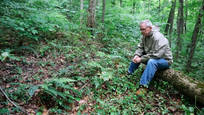 Ed Evans, Democratic West Virginia delegate and retired public school teacher, sits beside a sunken grave in the unmarked cemetery where more than 80 coal miners killed in the 1912 Jed Coal and Coke Company disaster are buried in Havaco, W.Va., on June 7, 2022.
