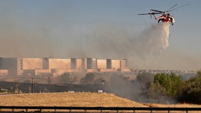 A helicopter drops water on flames from the Alturas Fire across Powers Blvd. from the Amazon Distribution Center on Thursday, May 12, 2022.
