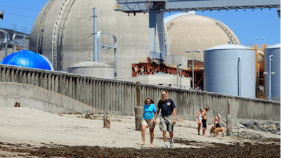 People walk on the sand near the shuttered San Onofre nuclear power plant in San Clemente, Calif., on June 30, 2011.