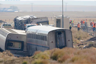 Workers stand near train tracks, Sept. 27, 2021, next to overturned cars from an Amtrak train that derailed a few days prior near Joplin, Mont., killing three people and injuring others.