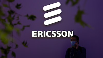A man wearing a face mask talks on his smartphone near a booth from Swedish technology firm Ericsson at the PT Expo in Beijing, Wednesday, Oct. 14, 2020.