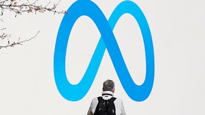 A person stands in front of a Meta sign outside of the company's headquarters in Menlo Park, Calif., Tuesday, March 7, 2023. Facebook’s parent Meta will slash another 10,000 jobs and will not fill 5,000 open positions as the social media pioneer cuts costs.