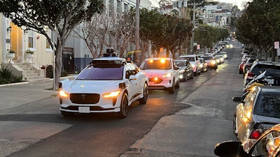 A Waymo driverless taxi stops on a street in San Francisco for several minutes because the back door was not completely shut, while traffic backs up behind it, on Feb. 15, 2023.