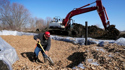 A worker shovels wood chips in a bioreactor trench in a farm field, Tuesday, March 28, 2023, near Roland, Iowa.