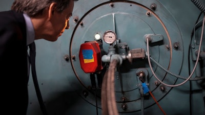 Josh London, senior vice president at Glenwood Management Corp., peers into the port hole of a natural gas fired boiler, located in the basement of The Grand Tier luxury apartment building, that his company uses to produce liquid carbon dioxide, Tuesday, April 18, 2023, in New York.