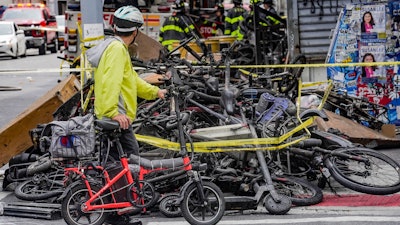 A biker stops to look at a pile of e-bikes in the aftermath of a fire in Chinatown, which authorities say started at an e-bike shop and spread to upper-floor apartments, Tuesday June 20, 2023, in New York.