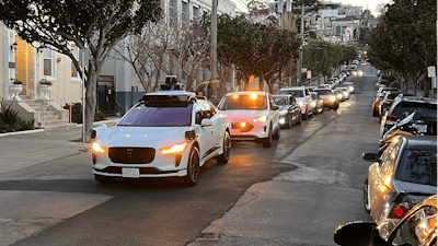 A Waymo driverless taxi stops on a street in San Francisco for several minutes because the back door was not completely shut, while traffic backs up behind it, on Feb. 15, 2023.