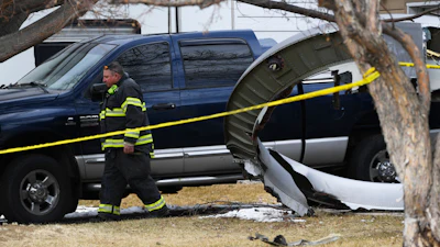 A North Metro firefighter walks past a large piece of a United airplane engine in the front yard of a home on Elmwood Street near E. 13th Avenue, Saturday, Feb. 20, 2021, in Broomfield, Colo.