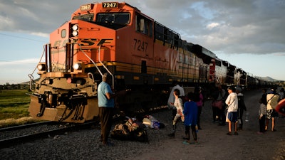 Migrants watch a train go past as they wait along the train tracks hoping to board a freight train heading north, one that stops long enough so they can hop on, in Huehuetoca, Mexico, Sept. 19, 2023.