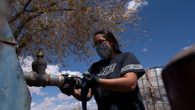 Raynelle Hoskie attaches a hose to a water pump outside a tribal office on the Navajo reservation, Tuba City, Ariz., April 20, 2020.