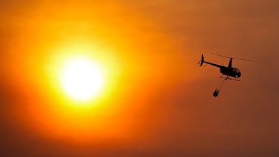 A helicopter carries a bucket as it flies over homes burned by the Smokehouse Creek Fire, Wednesday, Feb. 28, 2024, in Canadian, Texas.