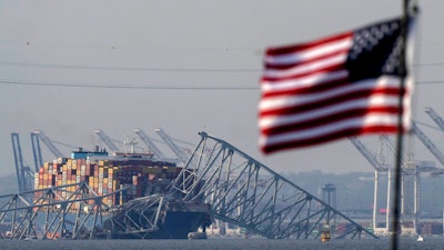 An American flag flies on a moored boat as the container ship Dali rests against wreckage of the Francis Scott Key Bridge, Tuesday, March 26, 2024, as seen from Pasadena, Md.