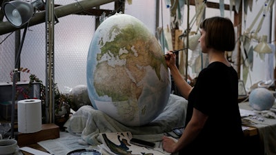 An artist paints a globe at a studio in London, Tuesday, Feb. 27, 2024.