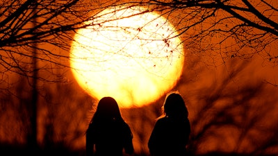 People watch the sunset at a park on an unseasonably warm day, Feb. 25, 2024, in Kansas City, Mo.