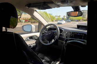 A Waymo minivan moves along a city street as an empty driver's seat and a moving steering wheel drive passengers during an autonomous vehicle ride, on April 7, 2021, in Chandler, Ariz.