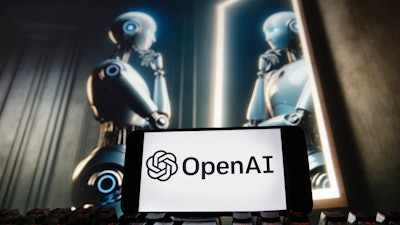 The OpenAI logo is displayed on a cellphone with an image on a computer monitor generated by ChatGPT's Dall-E text-to-image model.